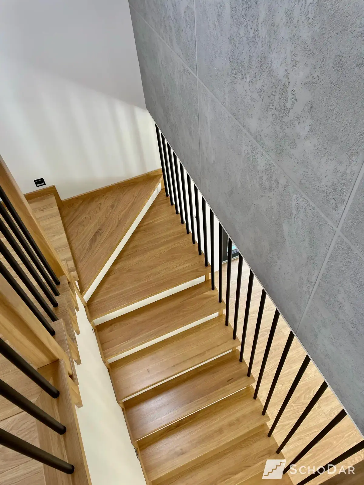 Zabiegowe schody drewniane z jasnego dębu z czarną metalową balustradą, widok z góry