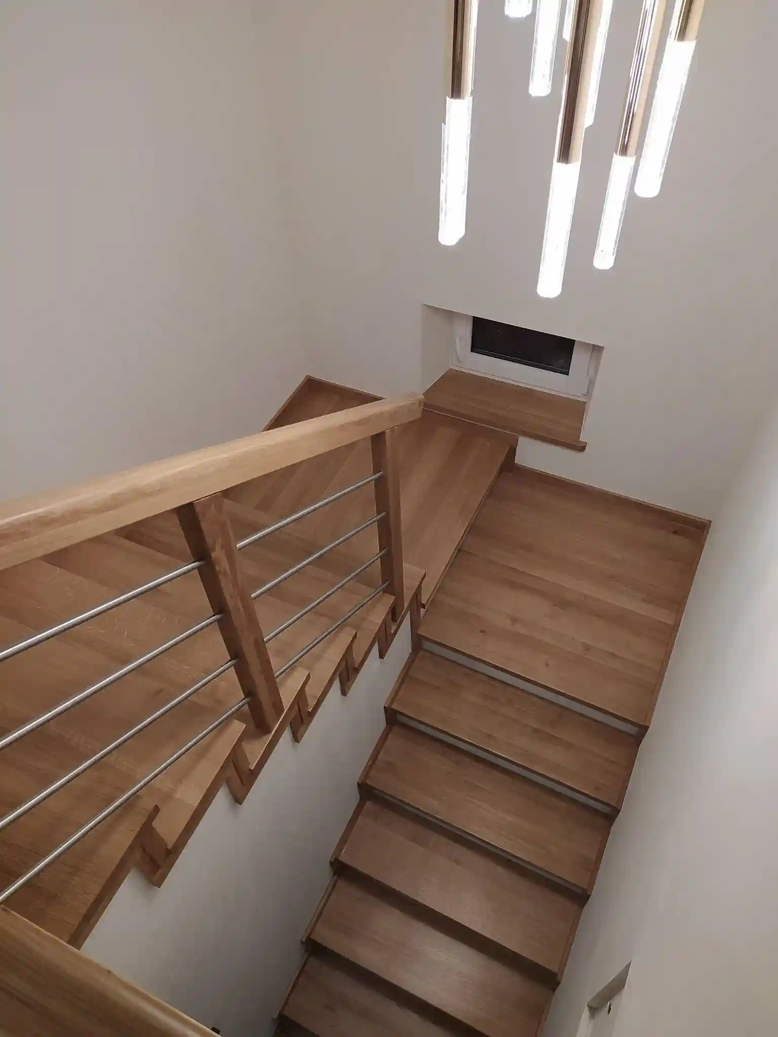 Klatka schodowa z jasnego drewna dębowego z podświetleniem sufitowym i stalową balustradą prętową